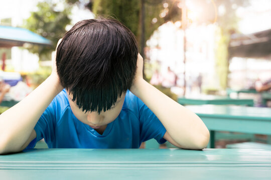 Close up of Asian autistic student child sit at table at school cover ears with hand and close eyes due to stress and anxiety. Autism stimming behavior for World Autism spectrum awareness day concept