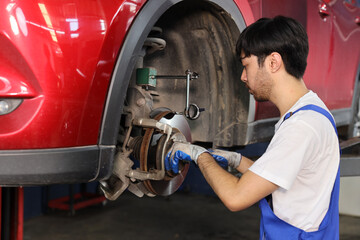 Man technician car mechanic in uniform checking or maintenance a lifted car service at repair garage station. Worker holding wrench and fixing brake discs. Concept of car center repair service.