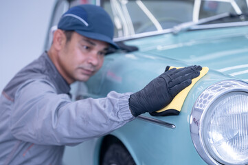Professional car service male worker, with orbital polisher, polishing green classic vintage car in...