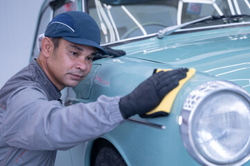 Professional car service male worker, with orbital polisher, polishing green classic vintage car in...