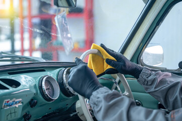 Professional car service male worker, with orbital polisher, polishing green classic vintage car in auto repair polishing shop