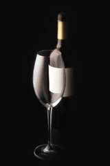 an empty wine glass and a bottle of red wine on a black background with an empty label . minimalistic still life studio vertical photo