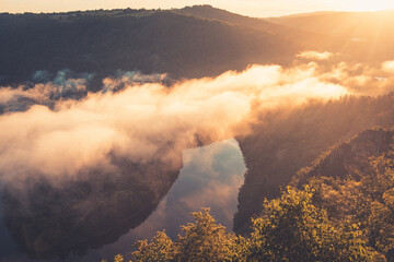 Fototapeta premium A Queuille en Auvergne, le belvédère modestement appelé le “Paradis”. Celui-ci donne sur la rivière Sioule qui forme le méandre de Queuille. vue à l'aube au lever du soleil avec de la brume