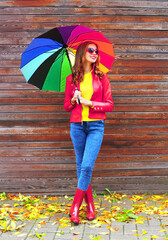 Autumn portrait of happy smiling young woman holding colorful umbrella wearing red jacket, rubber...