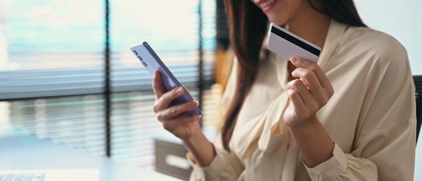Satisfied woman holding credit card, making payment on internet via smart phone. Online shopping, e-commerce concept