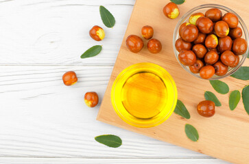 Fresh ripe jojoba fruit and jojoba oil in bowl on wooden table
