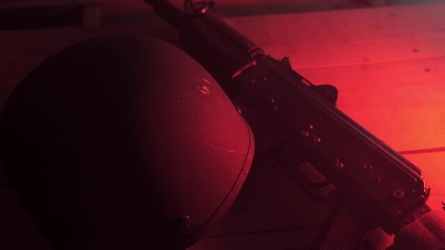 tactical helmet and  macine gun is lying on the table, close-up. smoke from gunshots. red alarm signalin armory room. indoor fighting. an attack on a checkpoint during the war. 