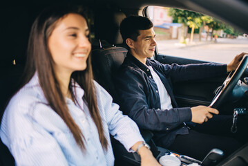 Enjoy travel. A beautiful young couple is sitting in the front passenger seat and smiling while a handsome man is driving a car