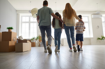 Fototapeta premium Family in their new home. Mom, dad and children enter a spacious modern light living room full of cardboard boxes. Backside view from behind. Mortgage, buying and moving house, real estate concept
