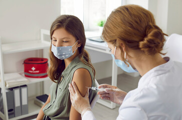 Doctor gives arm injection to child in medical face mask. Teenage school girl in facemask gets flu,...