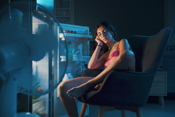 Woman suffering from the heat and sitting in front of the open fridge