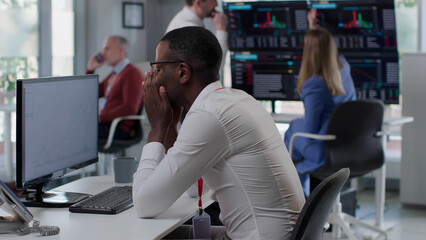 Fototapeta premium Side view of devastated African American manager sitting at desk in modern office