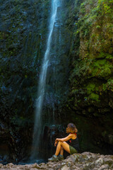 Unrecognizable young woman sitting in the waterfall at the Levada do Caldeirao Verde, Queimadas, Madeira