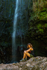 Fototapeta na wymiar A young woman at the waterfall at the end of the waterfall trail at Levada do Caldeirao Verde, Queimadas, Madeira
