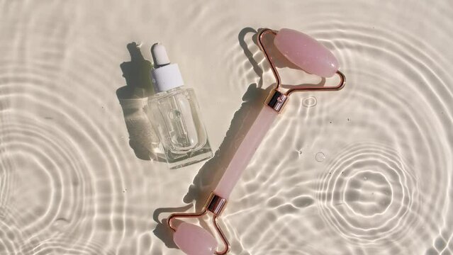 Cosmetic bottle with pipette and Massage roller on water with drops. Water with reflections sunlight and shadows. Women's cosmetics skincare. Sample of layout of beauty product. 4k 