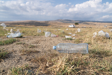 Rubbish from garbage dump spread by wind in rural area on summer day. Scattered plastic bottles and bags lie on grass in countryside causing pollution of environment. Ecological problem closeup view