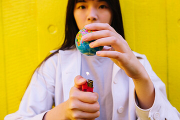 Young woman burning earth with cigarette lighter