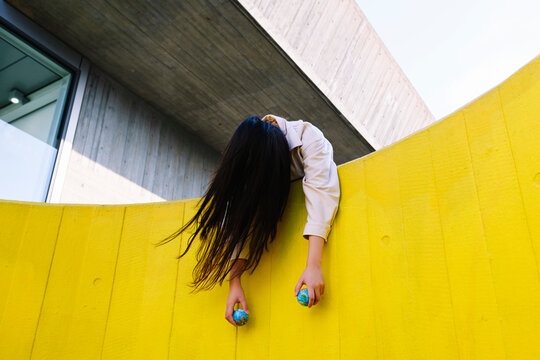 Unconscious young woman holding globes leaning on yellow wall