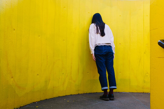 Depressed young woman leaning on yellow wall