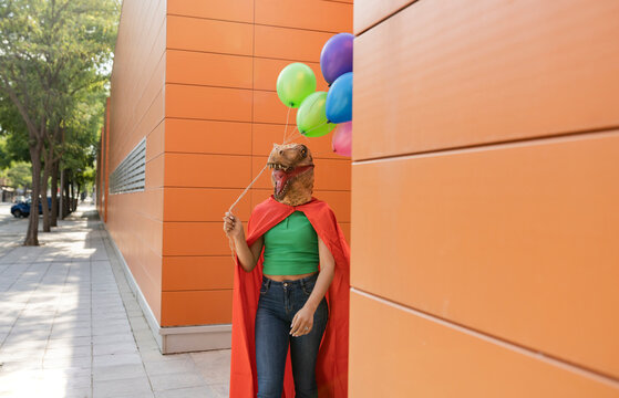 Woman wearing crocodile mask walking with multi colored balloons in front of wall