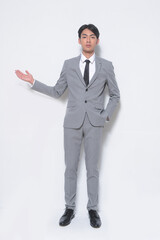 Full body young businessman wearing gray suit, white shirt ,black, tie with welcome gesture standing in studio