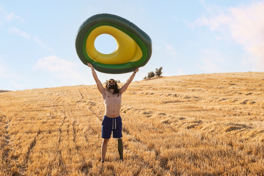 Shirtless man with prosthetic leg carrying inflatable ring at field on sunny day