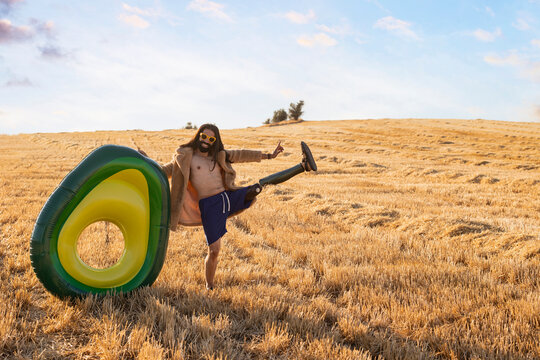 Happy hipster man with prosthetic leg balancing by inflatable ring at field on sunny day
