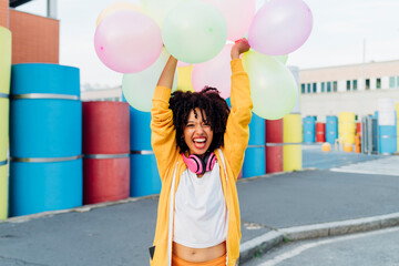 Happy young woman with arms raised holding colorful balloons