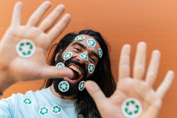Hipster man with recycling stickers on face and palms shouting in front of wall