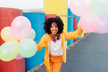 Smiling woman holding colorful balloons in front of pipes