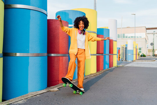 Cheerful woman enjoying skateboard by multi colored pipes