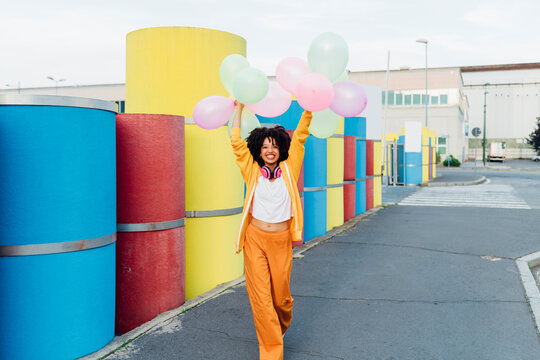 Happy woman holding colorful balloon walking on footpath