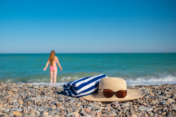 Hat, a towel and sunglasses. Tall woman with a long hair from a back is on a beach. Mediterranean sea with waves on the background. Blue and turquoise water. Vacation summer vibe. Slow motion video. 