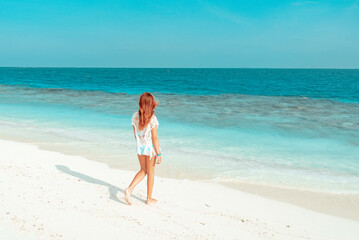 Fototapeta na wymiar red haired cute teenage girl in swimsuit and cape stands on shore of the Indian Ocean in Maldives island, summer vacation