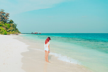 red haired cute teenage girl in swimsuit and cape stands on shore of the Indian Ocean in Maldives island, summer vacation