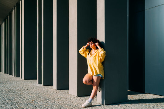 Woman listening music leaning on column at sunny day