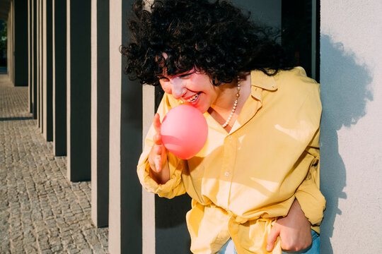 Smiling woman blowing bubble gum by column on sunny day