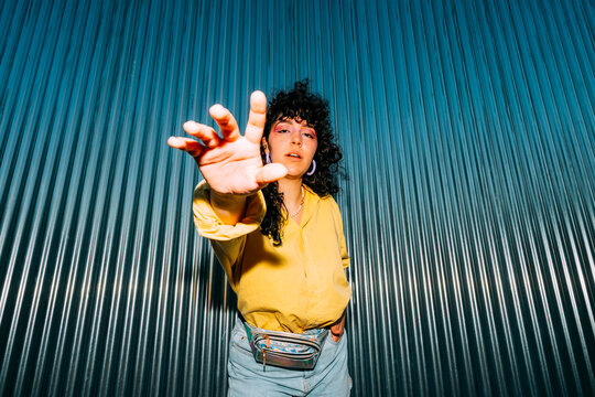 Young woman gesturing in front of corrugated wall
