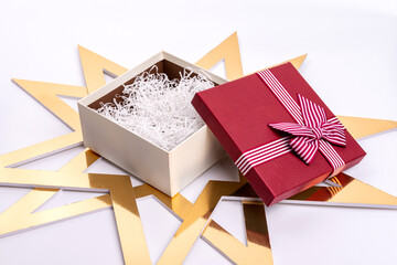 An open gift box with tinsel and a burgundy lid on a white background and gold large stars