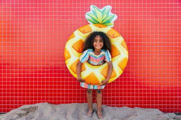 Smiling girl wearing swimming float standing in front of wall at beach