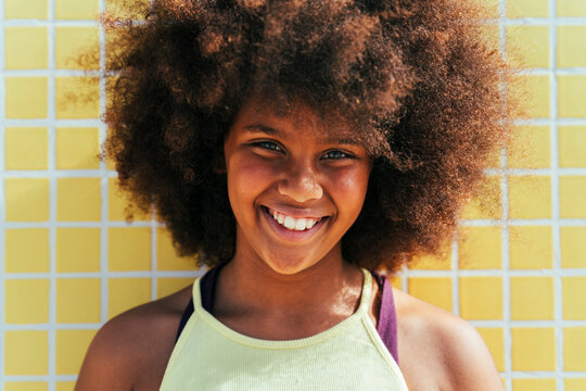 Happy girl with Afro hairstyle in front of yellow wall