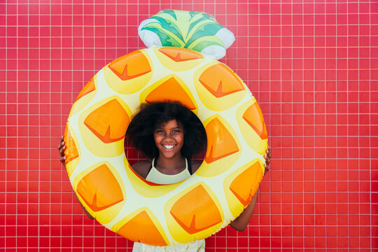 Happy girl holding swimming float standing in front of red wall