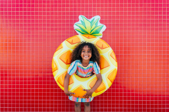 Cute girl wearing swimming float standing in front of red wall