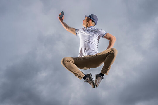 Man jumping and taking selfie through smart phone under cloudy sky