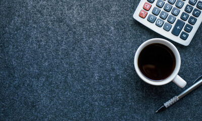 Flat lay view of cup of hot black coffee on gray felt desk mat with pen and calculator. 