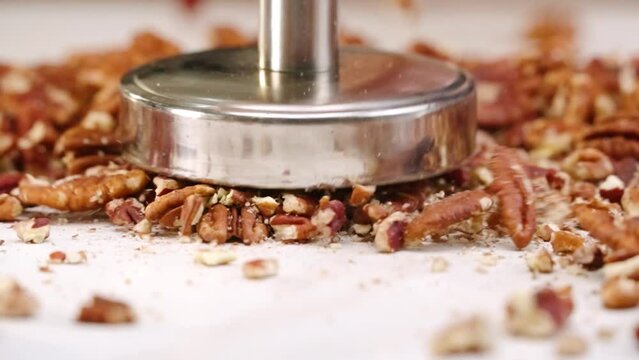 Whole pecan nuts being broken into tiny crushed pieces by mallet in slow motion