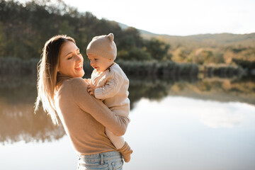 Smiling young woman holding playing with baby boy 1 year old wear knit clothes over nature...
