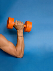 orange dumbbell in a strong sports male hand blue background photo