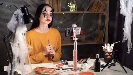 Beauty blogger woman on Halloween shoots a daily makeup tutorial near the camera on a tripod. Influencer live makeup review at home studio. Vlogger woman with brushes.