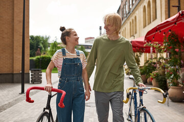 Fototapeta premium Young smiling caucasian couple walk with bicycles